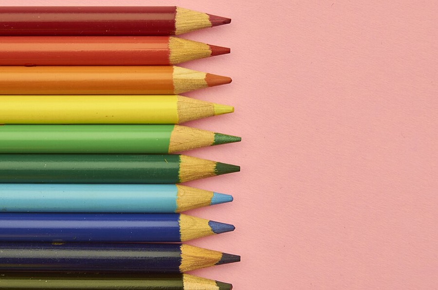 Lápices de colores alineados sobre fondo rosado